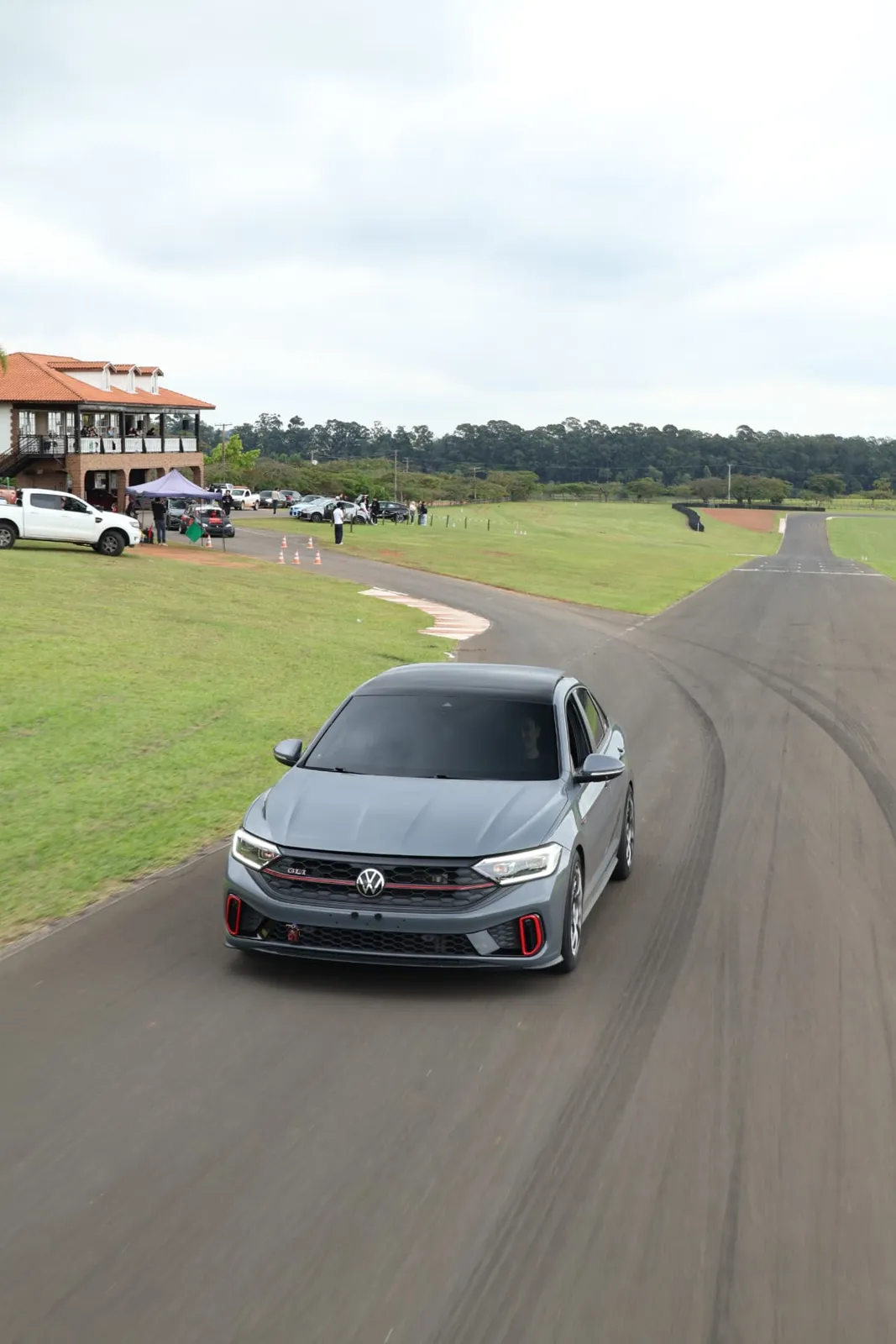 Volkswagen Jetta GLI cinza na pista com a sede ao fundo