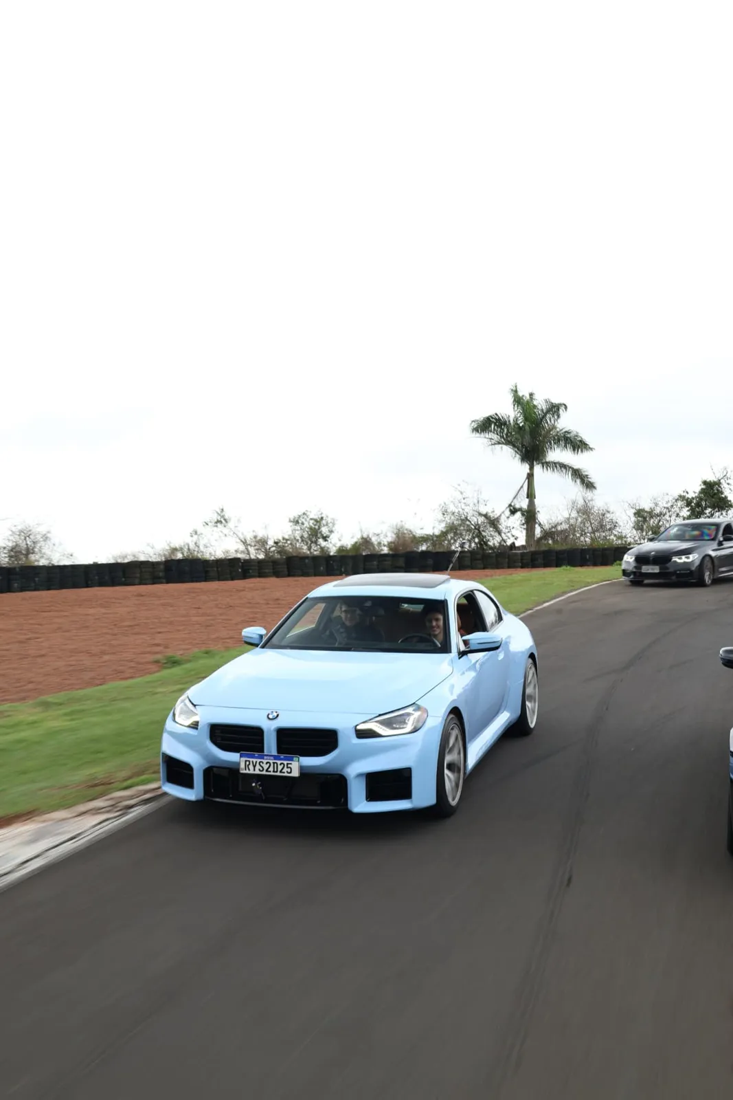 BMW M2 azul contornando a curva com a barreira de pneus ao fundo