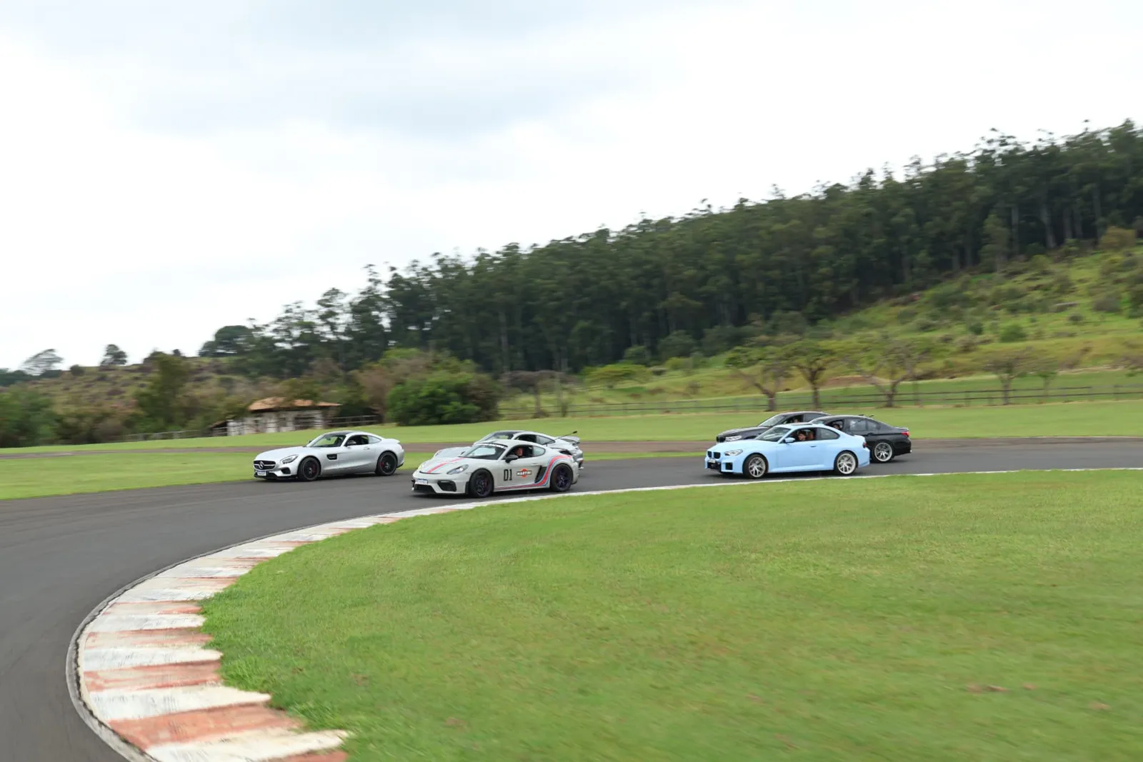 Pelotão contornando a curva com Mercedes-AMG GT, Porsche Cayman GT4 Martini e BMWs